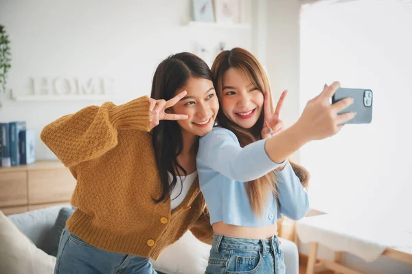 Two asian young women happy smiling and taking selfie in living room at home. Video call, Meeting conference