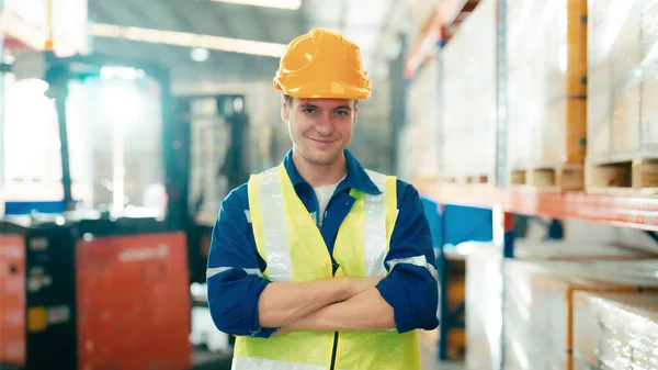 Handsome man and happy professional worker wearing safety vest and hard hat, Smiling to camera. Big warehouse with shelves full of stock