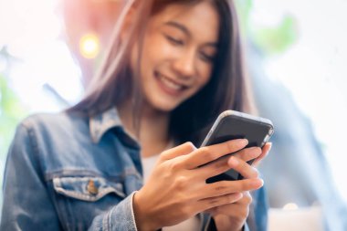 Genç Asyalı güzel bir kadın kafeteryada akıllı telefon kullanıyor, cep telefonuna, online alışverişe, transfer ödemesine, internet bankacılığına mesaj yazıyor.