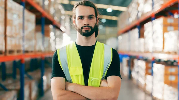 Handsome man and happy professional worker wearing safety vest, Smiling to camera. Big warehouse with shelves full of stock
