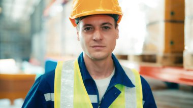 Handsome man and happy professional worker wearing safety vest and hard hat, Smiling to camera. Big warehouse with shelves full of stock