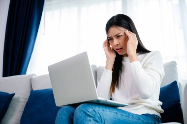 Ofis sendromu. Çok çalışan yorgun Asyalı kadın baş ağrısı çekiyor, bilgisayardan sonra görme sorunu yaşıyor. Evde yorgunluk çeken stresli genç bir kadın.
