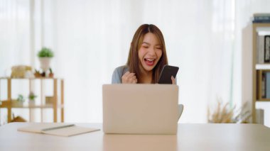 Asyalı bir kadının kazanmasını ya da bilgisayar laptopunda ecommerce alışveriş teklifi almasını kutlayan komik bir coşku. Heyecanlı mutlu kız kazanan başarıyı kutlayan deftere bakıyor.