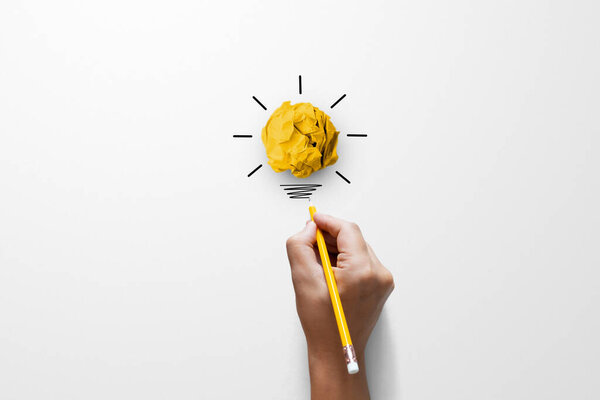Creative thinking ideas and innovation concept. Paper scrap ball yellow colour with light bulb symbol on white background and hand holding yellow pencil