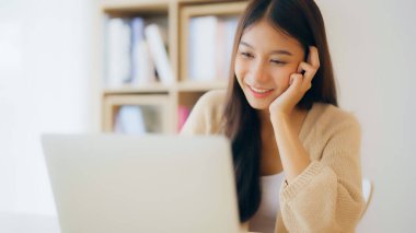 Evde çalışan genç Asyalı kadın. Evdeki masada bilgisayar kullanan mutlu bir kadın.
