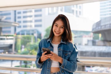 Sokakta yürüyen ve akıllı telefon kullanan genç Asyalı kadın.