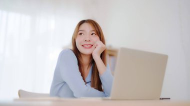 Evde çalışan genç Asyalı kadın. Evdeki masada bilgisayar kullanan mutlu bir kadın.