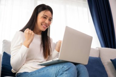 Asyalı bir kadının kazanmasını ya da bilgisayar laptopunda ecommerce alışveriş teklifi almasını kutlayan komik bir coşku. Heyecanlı mutlu kız kazanan başarıyı kutlayan deftere bakıyor.