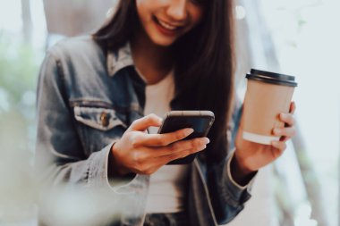 Genç Asyalı bir kadının rahat bir kafede oturup modern akıllı telefon cihazını kullanırken çekilmiş yakın plan görüntüsü. Kadın elleri cep telefonuyla mesaj yazıyor.