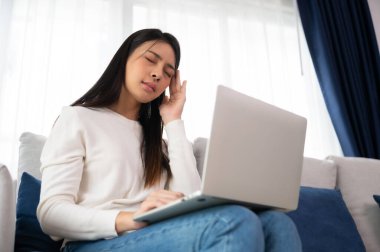 Ofis sendromu. Çok çalışan yorgun Asyalı kadın baş ağrısı çekiyor, bilgisayardan sonra görme sorunu yaşıyor. Evde yorgunluk çeken stresli genç bir kadın.