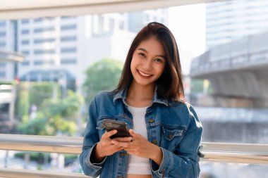 Sokakta yürüyen ve akıllı telefon kullanan genç Asyalı kadın.