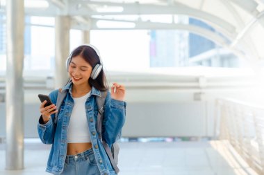Genç Asyalı kadın güzel müzik dinlemek ve şehirde yürümek için kulaklık kullanıyor. Kız mutluluğu, gülen surat. Kadın aşkı onu rahatlatan ve hayattan zevk alan müziği dinler.