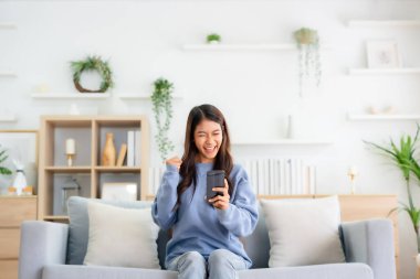 Happy young asian woman relax on comfortable couch at home texting messaging on smartphone, smiling girl use cellphone, chatting online message, shopping online from home