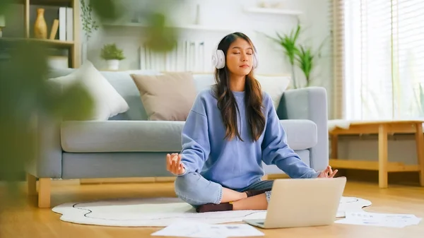 快乐的年轻亚洲女人在家里练习瑜伽和冥想 坐在客厅的地板上 保持着荷花的姿势 闭着眼睛放松 念念不忘和幸福概念 免版税图库照片