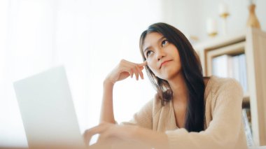 Bilgisayarda çalışan Asyalı genç bir kadın evdeki oturma odasında masa başında çalışıyor.