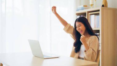 Asyalı bir kadının kazanmasını ya da bilgisayar laptopunda ecommerce alışveriş teklifi almasını kutlayan komik bir coşku. Heyecanlı mutlu kız kazanan başarıyı kutlayan deftere bakıyor.