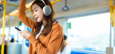 Genç Asyalı Kadın Yolcu ve Dinleyen Müzik Subway Sky Train 'de cep telefonu kullanıyor. Şehir ve Şehir Hayatı 'nda Yaşam Tarzı. Ulaşım Konsepti