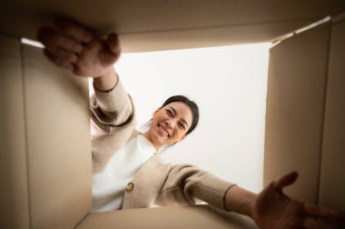 Bavulları boşaltan Asyalı genç bir kadın. Kutuyu açıp içine bakmak. Paket kutusu, teslimat servisi. İnsan duyguları ve yüz ifadesi