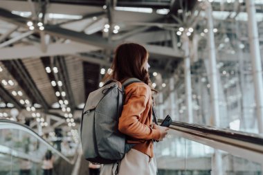 Uluslararası havaalanı terminalinde ya da modern tren istasyonunda çalışan Asyalı genç bir kadın. Sırt çantalı yolcu yürüyen yürüyen merdivende yürüyen kadın yolcu.