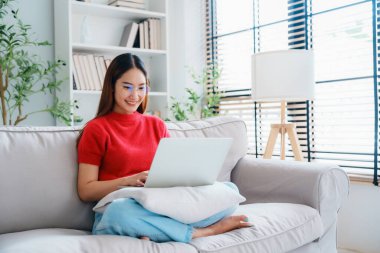 Evdeki kanepede otururken gözlük takan mutlu bir Asyalı kadın.