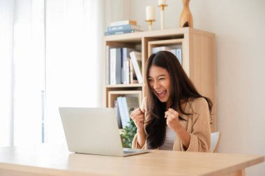 Mutlu Asyalı genç kadın kazanmayı kutluyor ya da bilgisayardan ekommerce alışveriş teklifi alıyor. Heyecanlı mutlu kız kazanan başarıyı kutlayan deftere bakıyor.