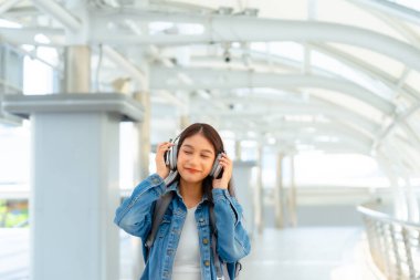 Genç Asyalı kadın güzel müzik dinlemek ve şehirde yürümek için kulaklık kullanıyor. Kız mutluluğu, gülen surat. Kadın aşkı onu rahatlatan ve hayattan zevk alan müziği dinler.