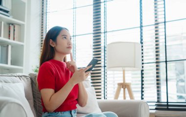 Mutlu genç Asyalı kadın rahat bir kanepede rahat rahat oturup akıllı telefonuna mesaj atıyor, gülümseyen kız cep telefonu sohbetini kullanıyor, evde online alışveriş yapıyor, video bağlantısı kuruyor.