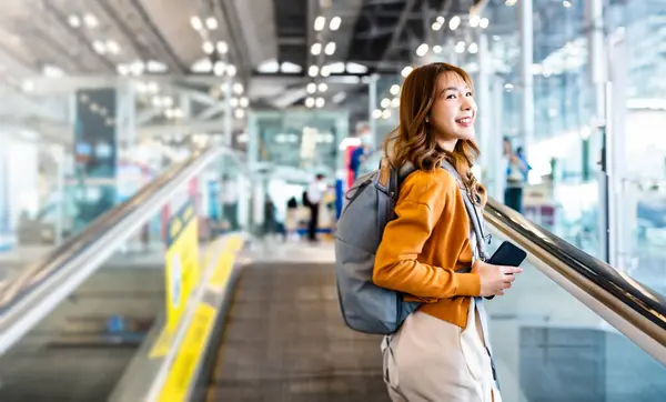 在国际机场候机楼或现代火车站工作的年轻亚洲妇女 背包客在自动扶梯上行走的女乘客 图库照片