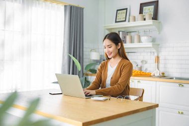 Ev mutfağında dizüstü bilgisayarla çalışan güzel bir Asyalı kadın. Evde çalış. Uzaktan eğitim, sanal eğitim, E-öğrenme, çevrimiçi eğitim, evde giysi
