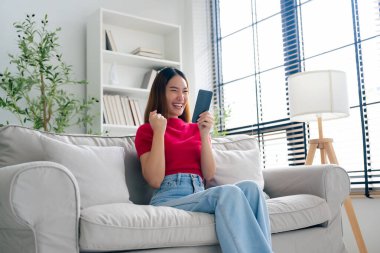 Happy young asian woman relax on comfortable couch at home texting messaging on smartphone, smiling girl use cellphone, chatting online message, shopping online from home