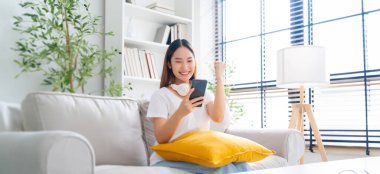 Happy young asian woman relax on comfortable couch at home texting messaging on smartphone, smiling girl use cellphone, chatting online message, shopping online from home