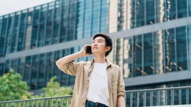 Akıllı telefon kullanan yakışıklı Asyalı öğrencinin portresi. Dışarıda duran genç bir adam elinde cep telefonuyla gülümsüyor.