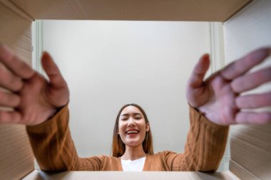 Şaşırmış Asyalı genç bir kadının bavullarını boşaltma açısı düşük. Kutuyu açıp içine bakmak. Paket kutusu, teslimat servisi. İnsan duyguları ve yüz ifadesi