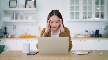 Ofis sendromu. Çok çalışan yorgun Asyalı kadın baş ağrısı çekiyor, bilgisayardan sonra görme sorunu yaşıyor. Evde yorgunluk çeken stresli genç bir kadın.