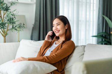 Mutlu genç Asyalı kadın rahat koltuğunda rahatla akıllı telefonuna mesaj at, gülümseyen kız cep telefonu sohbetini kullan