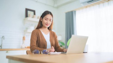 Ev mutfağında dizüstü bilgisayarla çalışan güzel bir Asyalı kadın. Evde çalış.