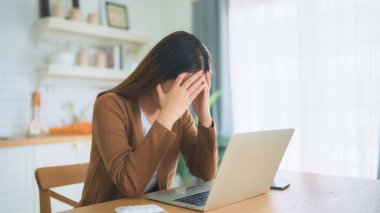 Ofis sendromu. Çok çalışan yorgun Asyalı kadın baş ağrısı çekiyor, bilgisayardan sonra görme sorunu yaşıyor. Evde yorgunluk çeken stresli genç bir kadın.