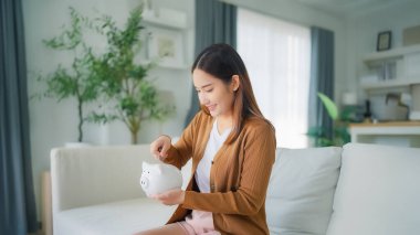 Genç Asyalı kadın kumbaraya para koyuyor. Para ve mali yatırım tasarrufu