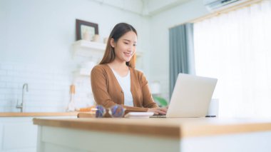 Ev mutfağında dizüstü bilgisayarla çalışan güzel bir Asyalı kadın. Evde çalış.