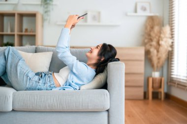 Mutlu, pozitif, genç, Asyalı bir kadın evde telefonda, gülümseyen bir kız. Uygulama kullanıyor ve internette akıllı telefonuyla kanepeye uzanıyor.