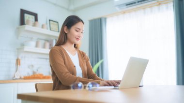 Ev mutfağında dizüstü bilgisayarla çalışan güzel bir Asyalı kadın. Evde çalış.