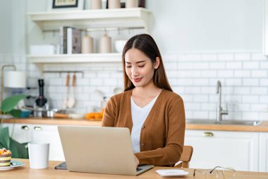 Ev mutfağında dizüstü bilgisayarla çalışan güzel bir Asyalı kadın. Evde çalış.