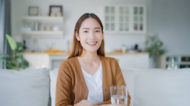 Oturma odasında kanepede oturmuş gülümseyen Asyalı genç bir kadının portresi ve mutlu bir yüz ifadesi.