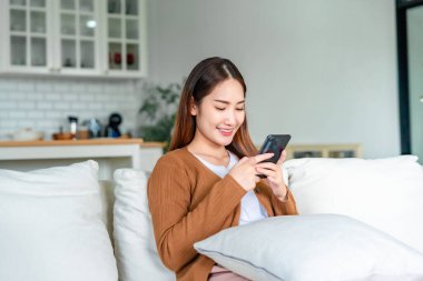 Mutlu genç Asyalı kadın rahat koltuğunda rahatla akıllı telefonuna mesaj at, gülümseyen kız cep telefonu sohbetini kullan