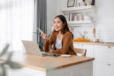 Ev mutfağında dizüstü bilgisayarla çalışan güzel bir Asyalı kadın. Evde çalış.