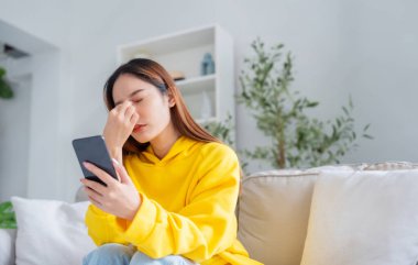 Cihaz ekranında kötü haber var. İşle ya da ilişkilerle ilgili sorunlardan bıkmış Asyalı bir kadın kanepeye oturmuş, umutsuzluk ve endişe duyuyor, yalnızlık çekiyor, psikolojik sorunlar yaşıyor.