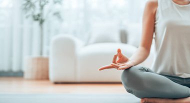Evde yoga ve meditasyon yapan Asyalı bir kadının lotus pozisyonunda oturma odasında oturduğu eli yakın. Dikkatli meditasyon ve refah kavramı