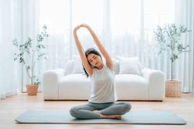Mutlu genç Asyalı kadın yoga ve omuz egzersizi yapıyor. Oturma odasında yerde oturuyor.