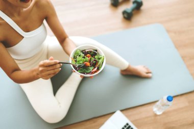 Salata kasesi tutan ve kameraya bakan genç Asyalı kadın. Spor giyimli güzel bir kız evde egzersiz yaptıktan sonra temiz sebze yemekten hoşlanır. Diyet ve Sağlıklı Yemek Konsepti