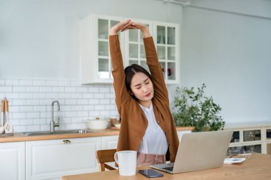 Ofis sendromu konsepti. Bilgisayarda uzun süre çalıştıktan sonra boyun ve omuz ağrısı çeken Asyalı genç bir kadın. Kaslarını gevşetmek için esniyor.